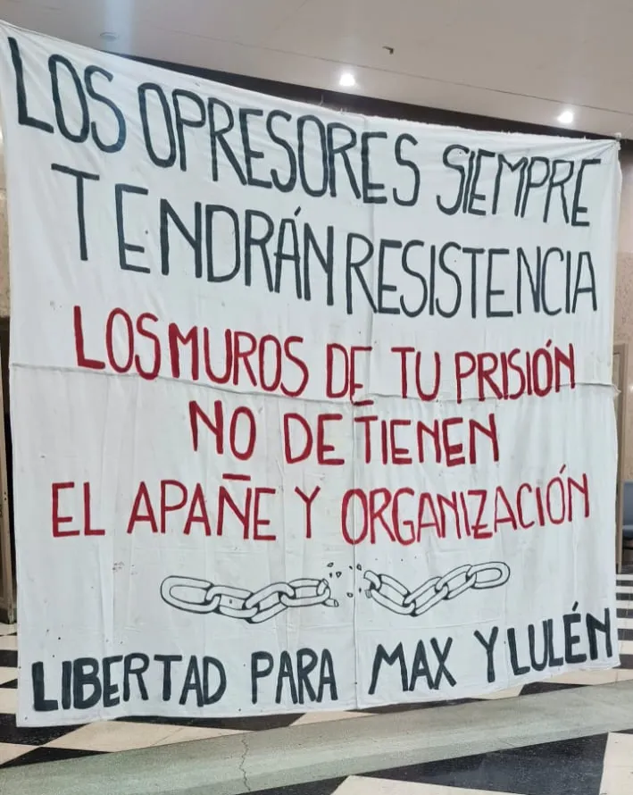 Foto de una bandera con tela blanca y texto que dice 'Los opresores siempre tendrán resistencia. Los muros de tu prisión no detienen el apañe y organización', dibujo de eslabones de una cadena rota, y texto que dice 'Libertad para Max y Lulen'