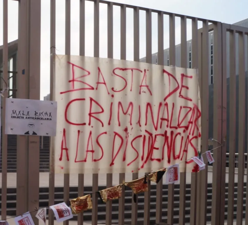 Foto de un cartel pegado en una reja que dice Basta de criminalizar a las disidencias